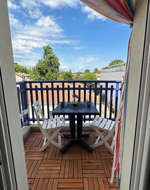 Eine Holzterrasse mit Tisch und Stühlen, einem Geländer und Blick auf Himmel und Bäume.