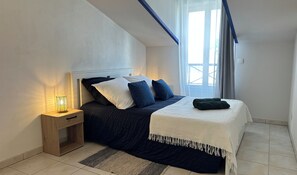 Een slaapkamer met een bed, nachtkastje, lamp en uitzicht op het omliggende landschap.