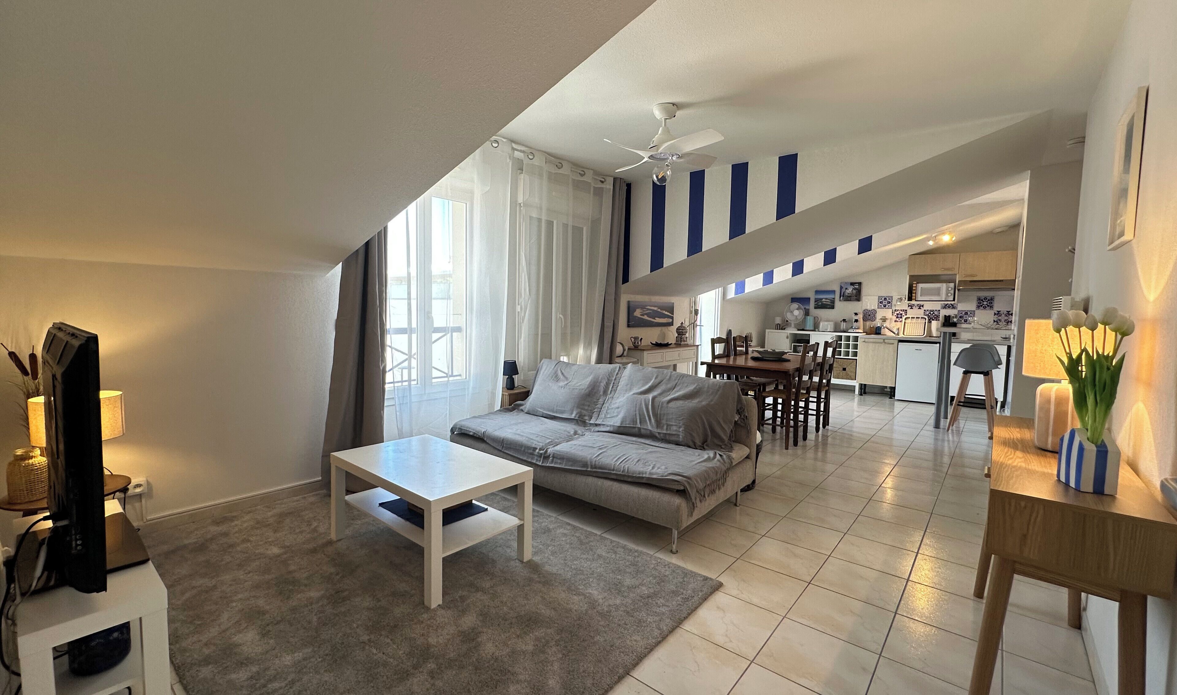 A modern living room with a sofa, a dining table, and a kitchen in the background.