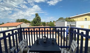 Ein Balkon mit Tisch und Stühlen, mit Blick auf eine Wohngegend mit Häusern und Bäumen.