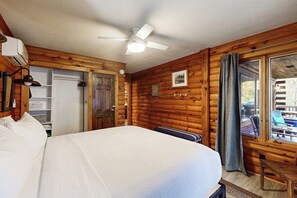 A log cabin room with a bed, a ceiling fan, a window with curtains, and a view of the outside. - 2BR lakefront with hot tub, dock, & 50ft shoreline (Dundee)