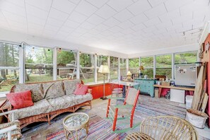 A sunlit room with a sofa, a dining table, and a kitchen area with a refrigerator. - Beautiful 3BR Riverfront Adirondacks - Hot Tub (Chestertown)