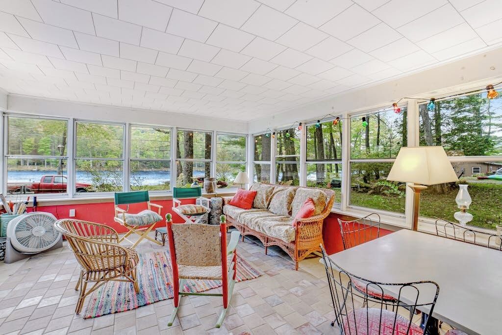 A sunroom with large windows, wicker furniture, and a view of a lake.