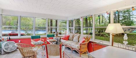 A sunroom with large windows, wicker furniture, and a view of a lake.