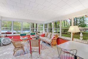 A sunroom with large windows, wicker furniture, and a view of a lake. - Beautiful 3BR Riverfront Adirondacks - Hot Tub (Chestertown)