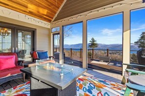 A spacious deck with a glass-top table, seating area, and a view of the mountains. - 5BR panoramic lake acreage - sauna, game tables (Bolton Landing)