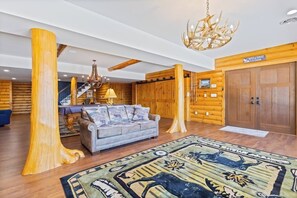 A log cabin interior with a sofa, chandelier, and a welcome sign. - 5BR panoramic lake acreage - sauna, game tables (Bolton Landing)