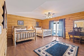 Interior de una cabaña de troncos con dos camas de madera, un ventilador de techo y una alfombra grande.