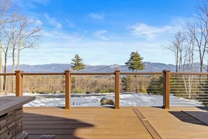 Una terraza de madera con barandilla metálica que domina un paisaje nevado con montañas al fondo.
