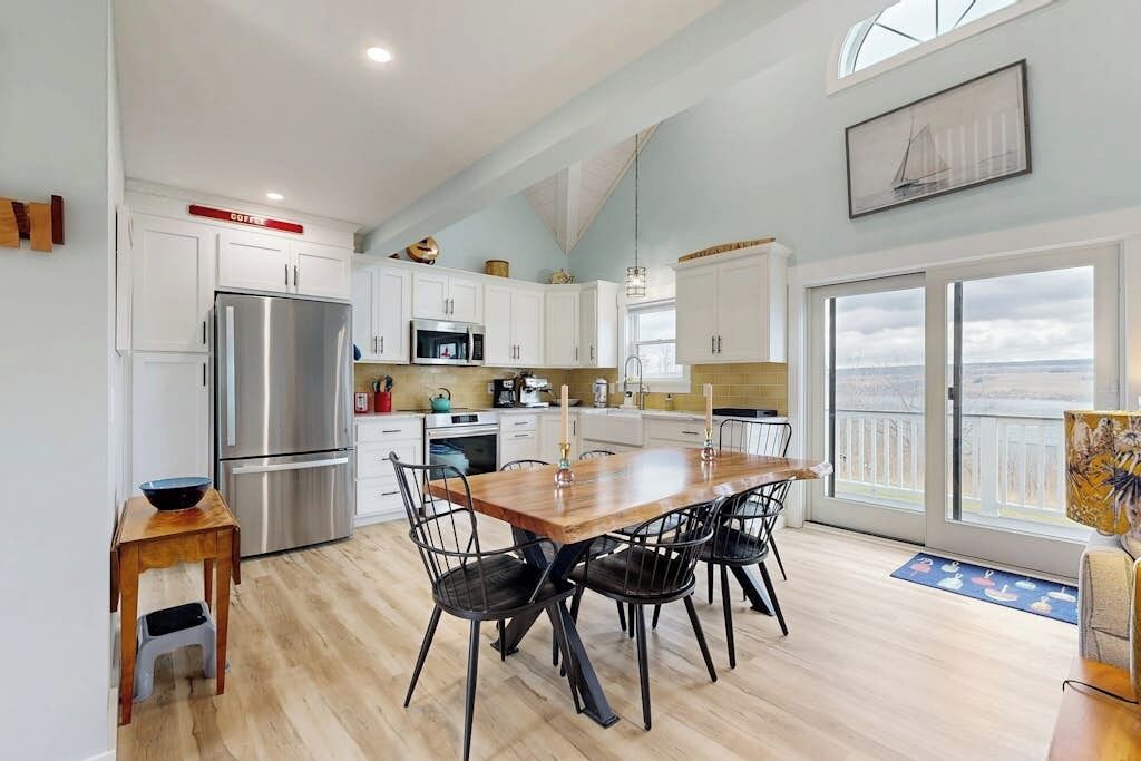 A modern kitchen with white cabinets, stainless steel appliances, and a dining area with a wooden table and chairs.