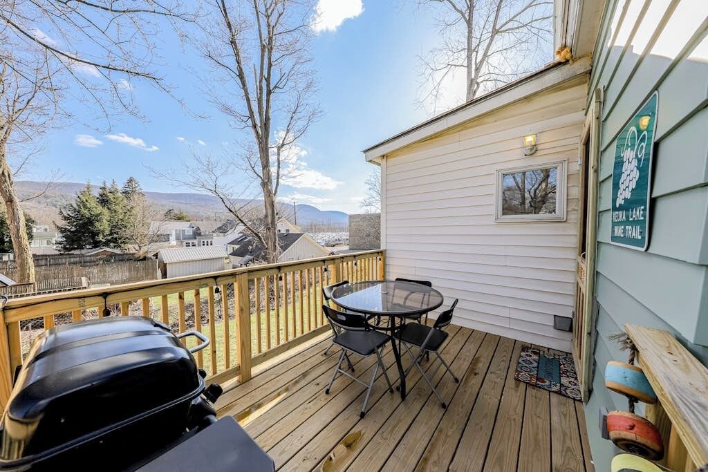 A deck with a grill, a table with chairs, and a view of a mountain range.