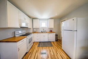 Eine kleine Küche mit weißen Schränken, einer Holz Arbeitsplatte, einem eingebauten Backofen und einem Kühlschrank.
