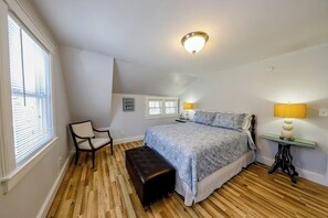 Ein Schlafzimmer mit einem Bett, einem Sessel, einer Bank, einem Nachttisch und einer Lampe.