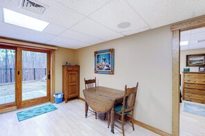 A dining area with a wooden table and chairs, a painting on the wall, and a sliding glass door leading to an outdoor area. - 3BR Home near lake withmedia room, fireplace, grill (Hague)