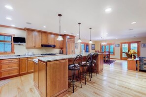 A spacious kitchen with wooden cabinets, a central island with bar stools, and pendant lighting. - 3BR Home near lake withmedia room, fireplace, grill (Hague)