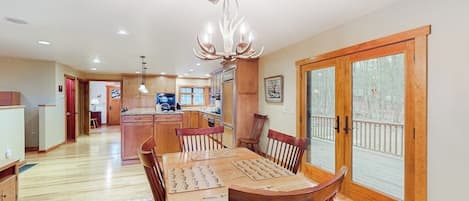 A dining area with a wooden table and chairs, a chandelier, and a view through a glass door.
