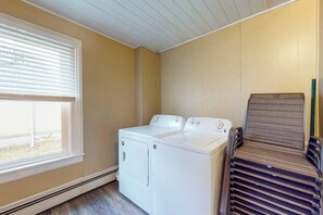 Un cuarto de lavandería con lavadora y secadora de carga frontal, una ventana con persianas y una pila de toallas dobladas.