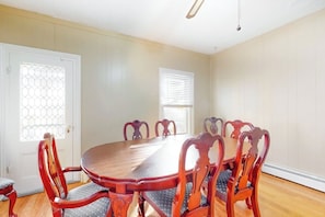 Comedor con mesa de madera y seis sillas, una puerta con ventanal y pared con ventana.