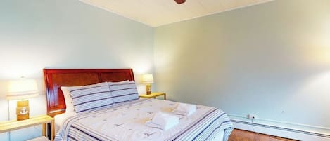 A bedroom with a wooden headboard, a bed with striped bedding, two bedside lamps, a ceiling fan, and a wooden floor.