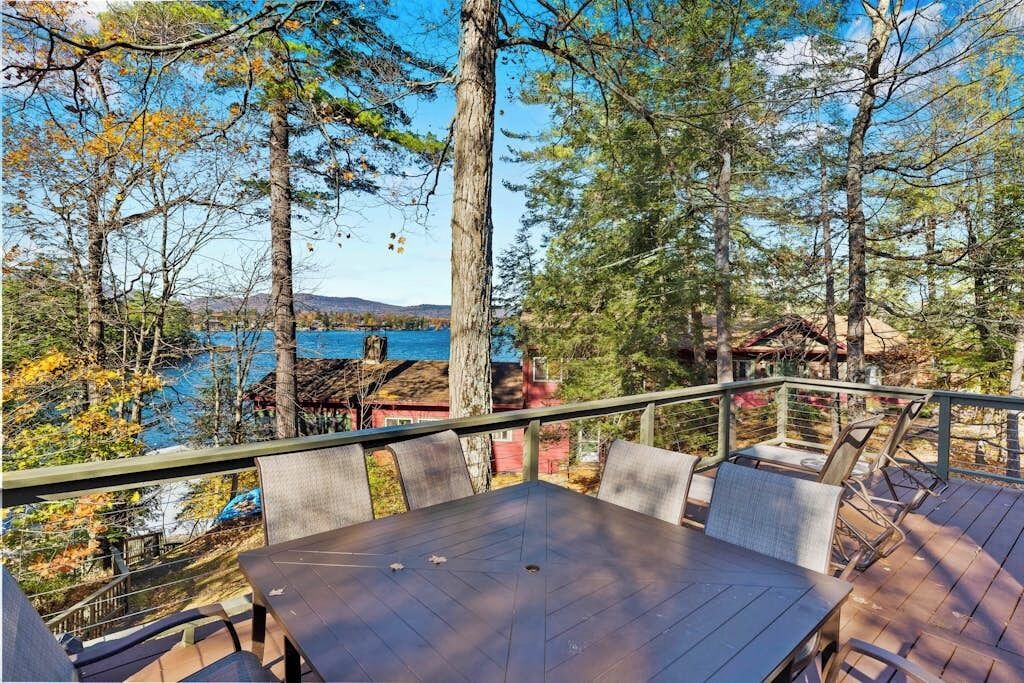 An outdoor deck with a table and chairs, overlooking a body of water and trees.