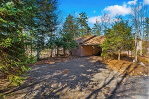 A rustic cabin with a dirt driveway, surrounded by dense trees and a clear sky. - Scenic lakefront 4BR with water access & dock (Kattskill Bay)