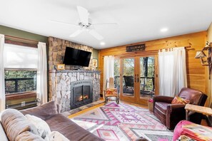 A cozy living room with a stone fireplace, a ceiling fan, and a sign indicating the location. - Scenic lakefront 4BR with water access & dock (Kattskill Bay)