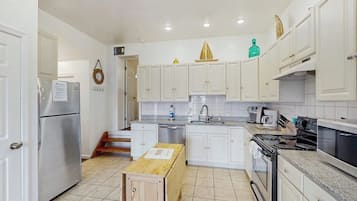 Una cocina compacta con gabinetes blancos, un refrigerador de acero inoxidable, estufa y pileta.