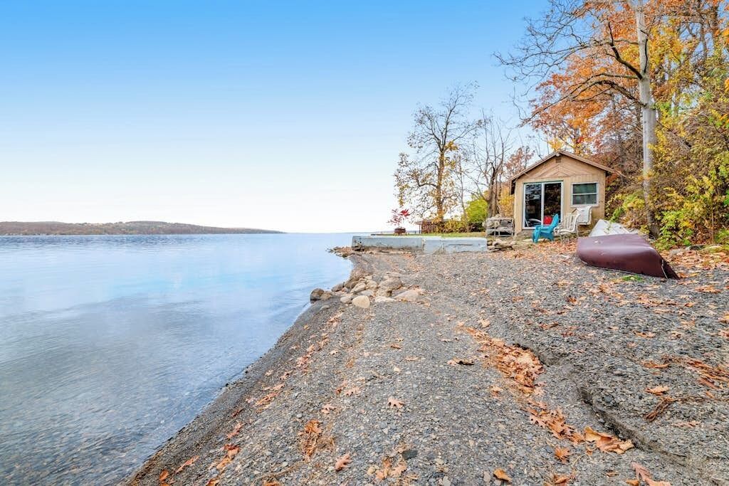 A lakeside property with a small cabin, a clear view of the water, and a gravel beach.