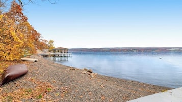 A lakeside view with a dock, a covered seating area, and a pebble beach.