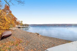 A lakeside view with a dock, a covered seating area, and a pebble beach.