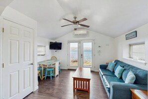 A room with a ceiling fan, a television mounted on the wall, a large window with a view, and a blue sofa.