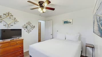 A bedroom with a bed, a wooden dresser, a ceiling fan, and a television.