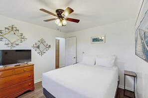 A bedroom with a bed, a wooden dresser, a ceiling fan, and a television.
