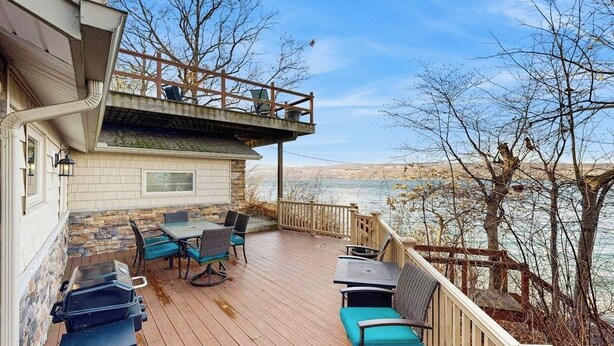 Um deck coberto com móveis de exterior, com vista para um corpo de água e uma paisagem montanhosa.