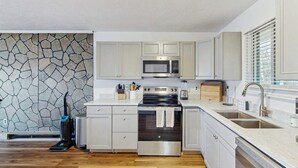 Uma cozinha moderna com armários brancos, painel de parede de pedra, micro-ondas embutido, fogão e máquina de lavar louça.