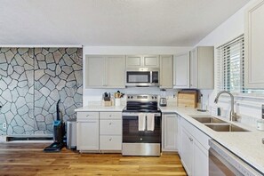 A modern kitchen with white cabinetry, a stone backsplash, a built-in microwave, a stove, and a dishwasher.