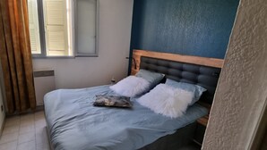 Ein Schlafzimmer mit einem Bett, einem Fenster mit Jalousien, einem Heizkörper und einer blauen Wand.