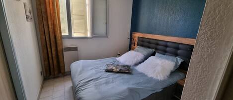 A bedroom with a bed, a window with blinds, a radiator, and a blue wall.