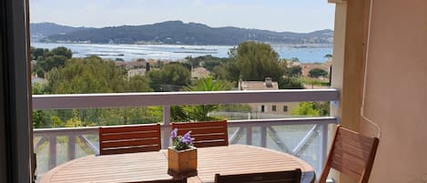 A balcony with a table and chairs, overlooking a scenic view of a body of water and hills.