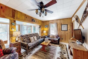 A cozy room with a wooden ceiling, a ceiling fan, a patterned sofa, a coffee table, and a television. - 3BR dog-friendly cottage with wrap-around deck (Chestertown)