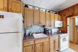 A kitchen with wooden cabinets, a white refrigerator, a microwave, a sink, and a stove. - 3BR dog-friendly cottage with wrap-around deck (Chestertown)