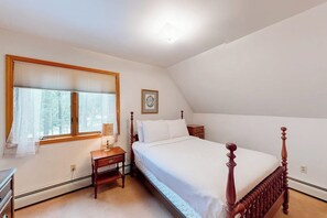 Ein Schlafzimmer mit einem Einzelbett, einem Nachttisch, einem Fenster mit Jalousien und einem gerahmten Bild an der Wand.