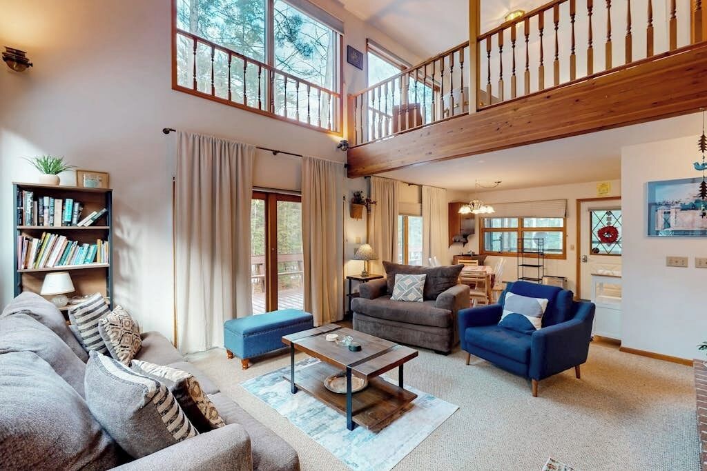 A spacious living room with a high ceiling, a wooden staircase, and a view of the outdoors.