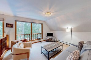 Ein geräumiges Wohnzimmer mit großem Fenster, einem Flachbildfernseher, einer Couch, einem Couchtisch und einer Treppe.