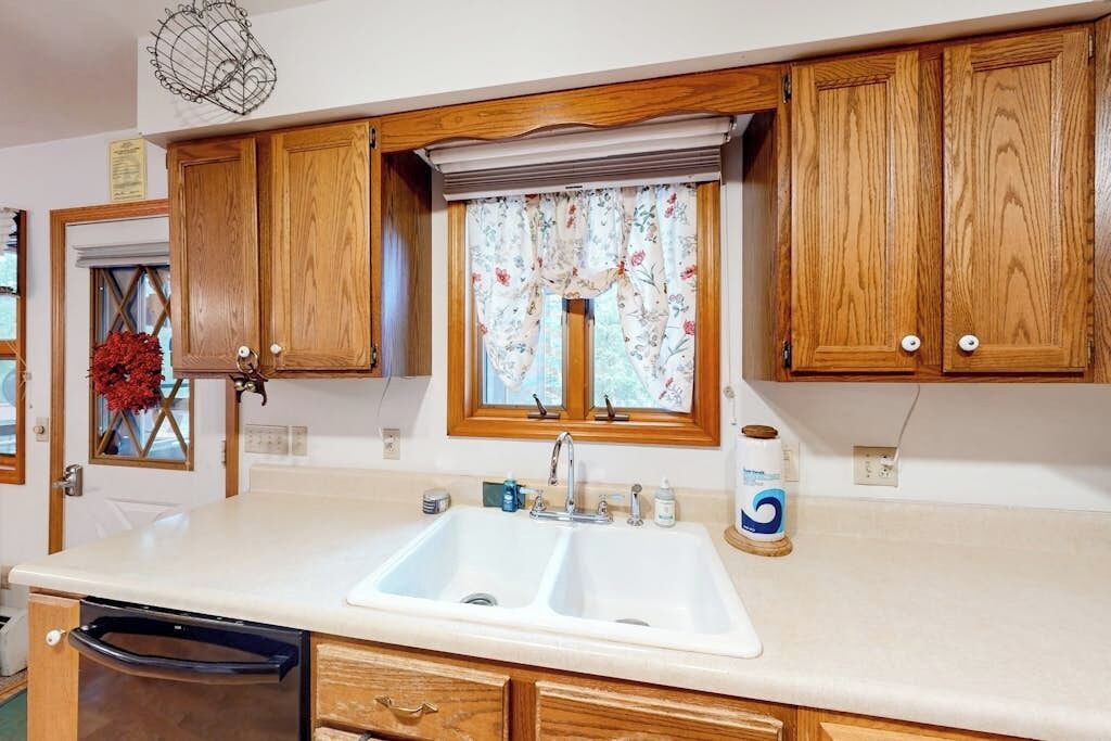 A kitchen with wooden cabinets, a double sink, and a window with floral curtains.