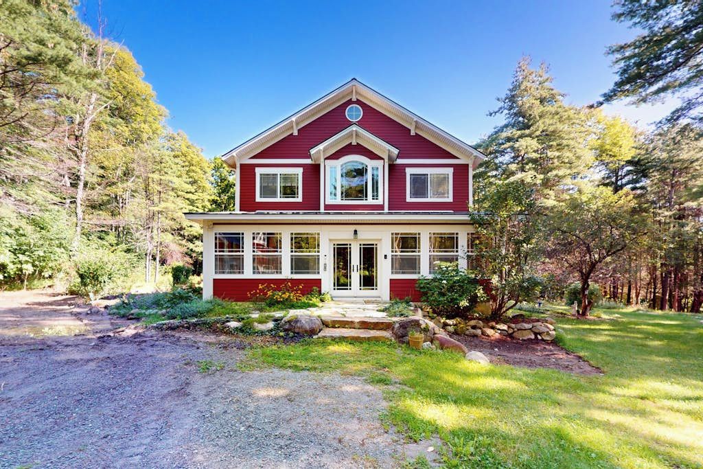 A two-story house with a red and white exterior, a front porch, and a stone foundation.