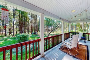 A covered porch with a view of a forest, a red railing, and a seating area with a table and chairs. - 4BR Green home near beach with firepit & fireplace (Hague)