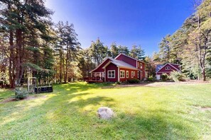 A red two-story house with a large front lawn and a small deck. - 4BR Green home near beach with firepit & fireplace (Hague)