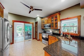A kitchen with a refrigerator, stove, microwave, and wooden cabinets. - 4BR Green home near beach with firepit & fireplace (Hague)