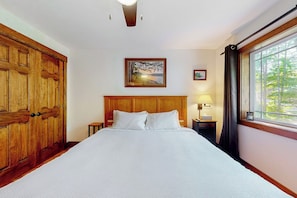 A hotel room with a large bed, wooden wardrobe, a nightstand with a lamp, a framed picture on the wall, and a window with curtains. - 4BR Green home near beach with firepit & fireplace (Hague)